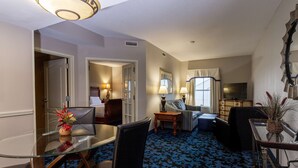 A hotel room with a glass dining table, two chairs, a sofa, a TV, and a patterned carpet.
