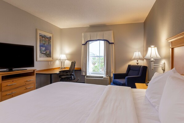 Une chambre d’hôtel équipée d’un lit, d’un bureau, d’une chaise, d’une télévision et d’une fenêtre avec des rideaux.