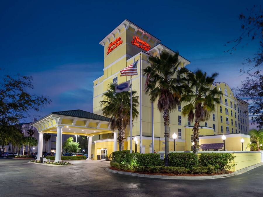 A hotel with a covered entrance, palm trees, and an American flag.