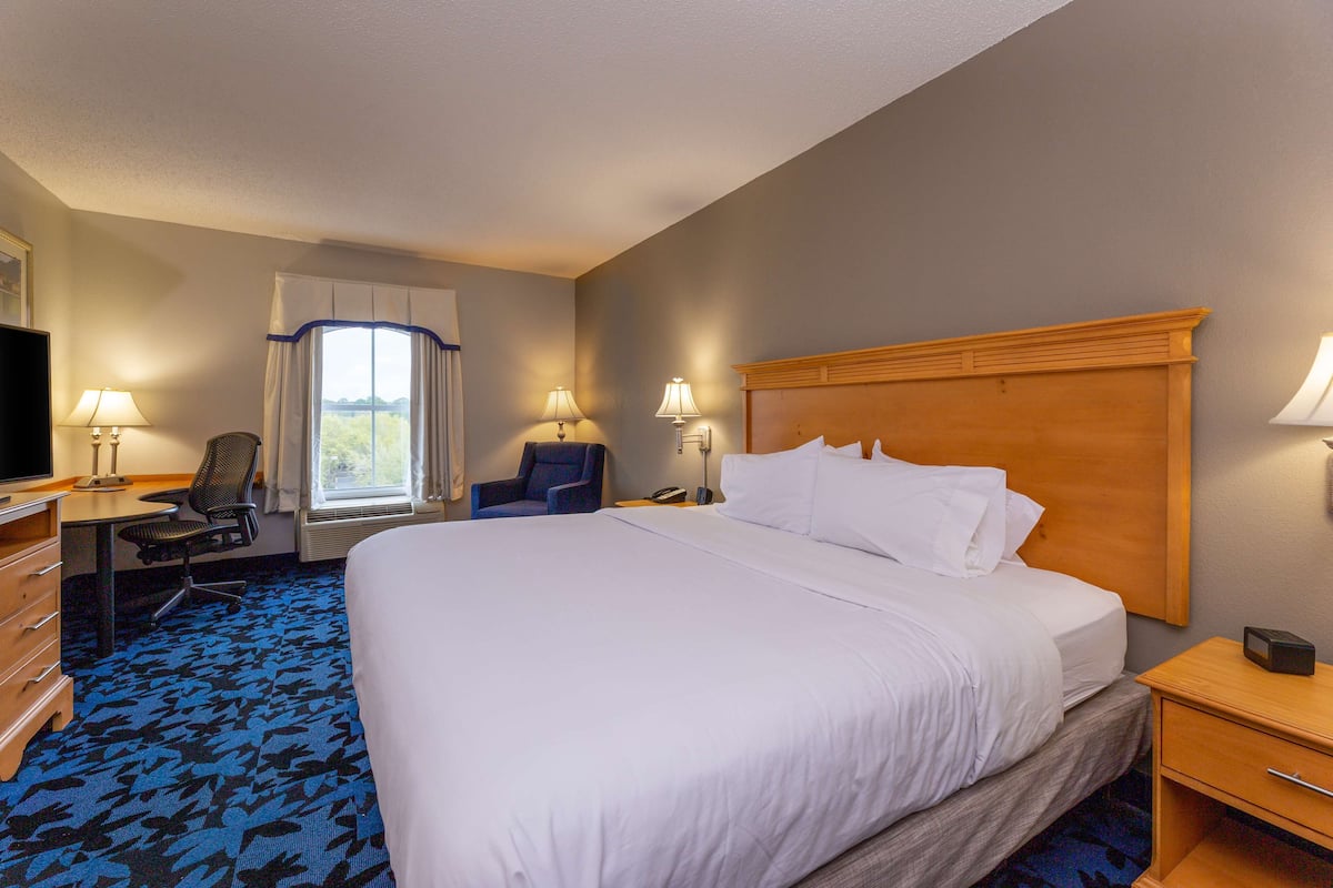 A hotel room with a large bed, a desk with a chair, a television, and a window with curtains.