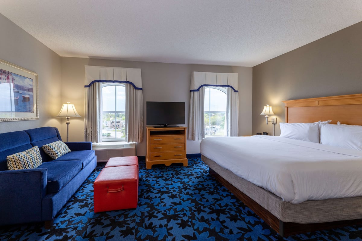 A hotel room with a bed, a sofa, a TV, a dresser, and a window with curtains.