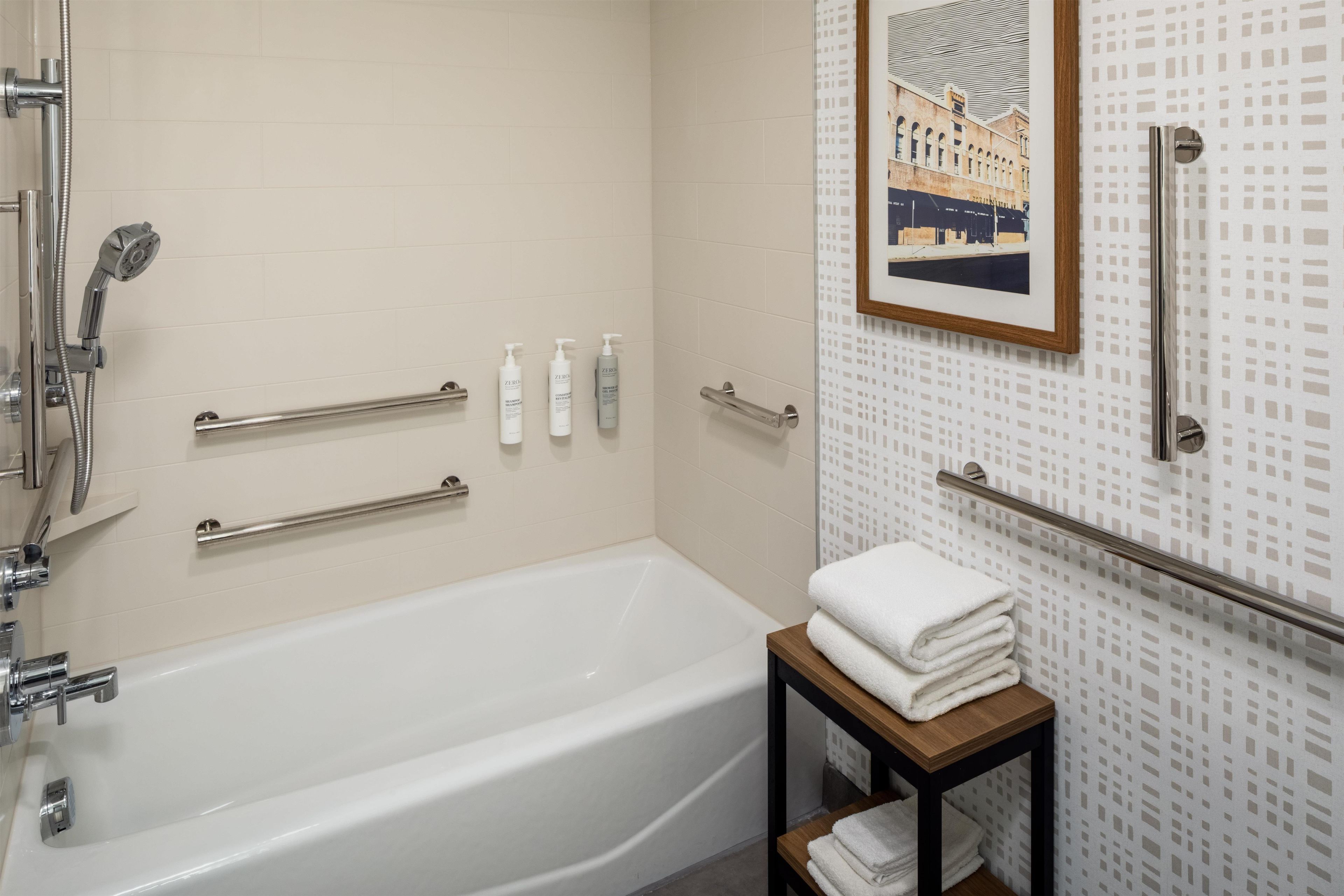 Une salle de bain moderne avec une baignoire blanche, des barres d’appui et un tableau encadré au mur.