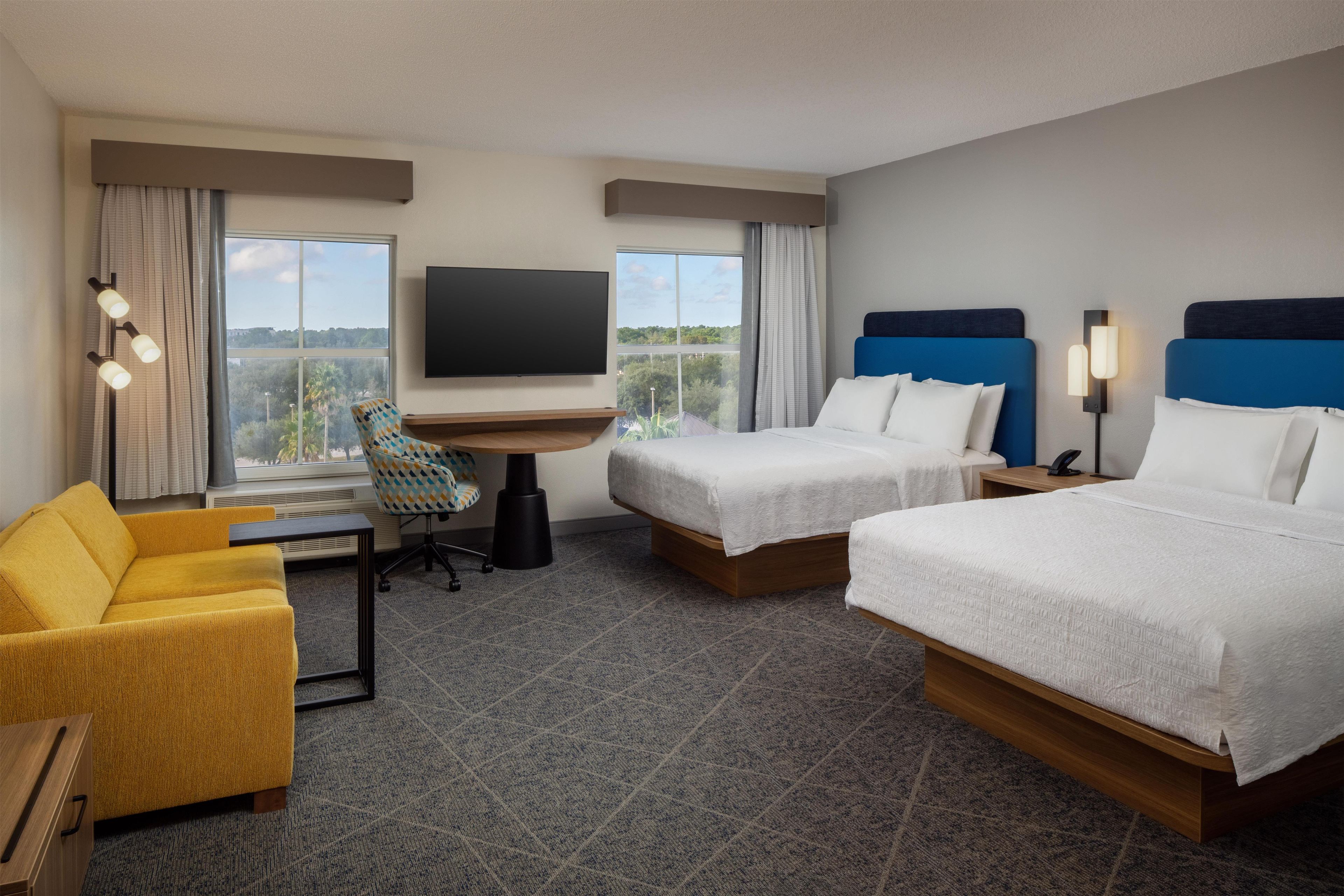 A hotel room with two beds, a desk, a chair, and a TV.