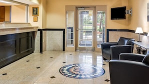 A hotel lobby with a reception desk, seating area, and a patterned floor. - Suburban Studios Avondale (Westwego)