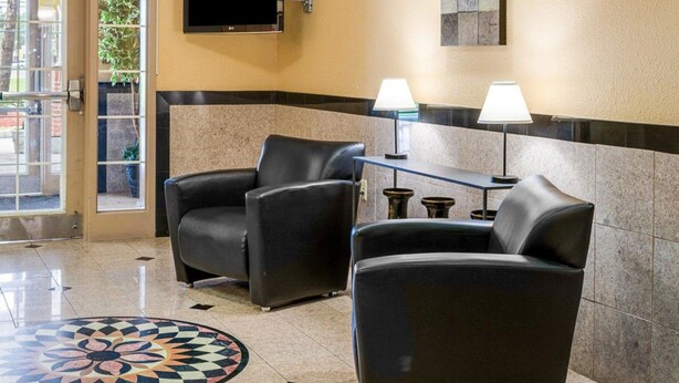 A lobby with two leather armchairs, a small table with lamps, a flat-screen TV, and a decorative floor pattern. - Suburban Studios Avondale (Westwego)