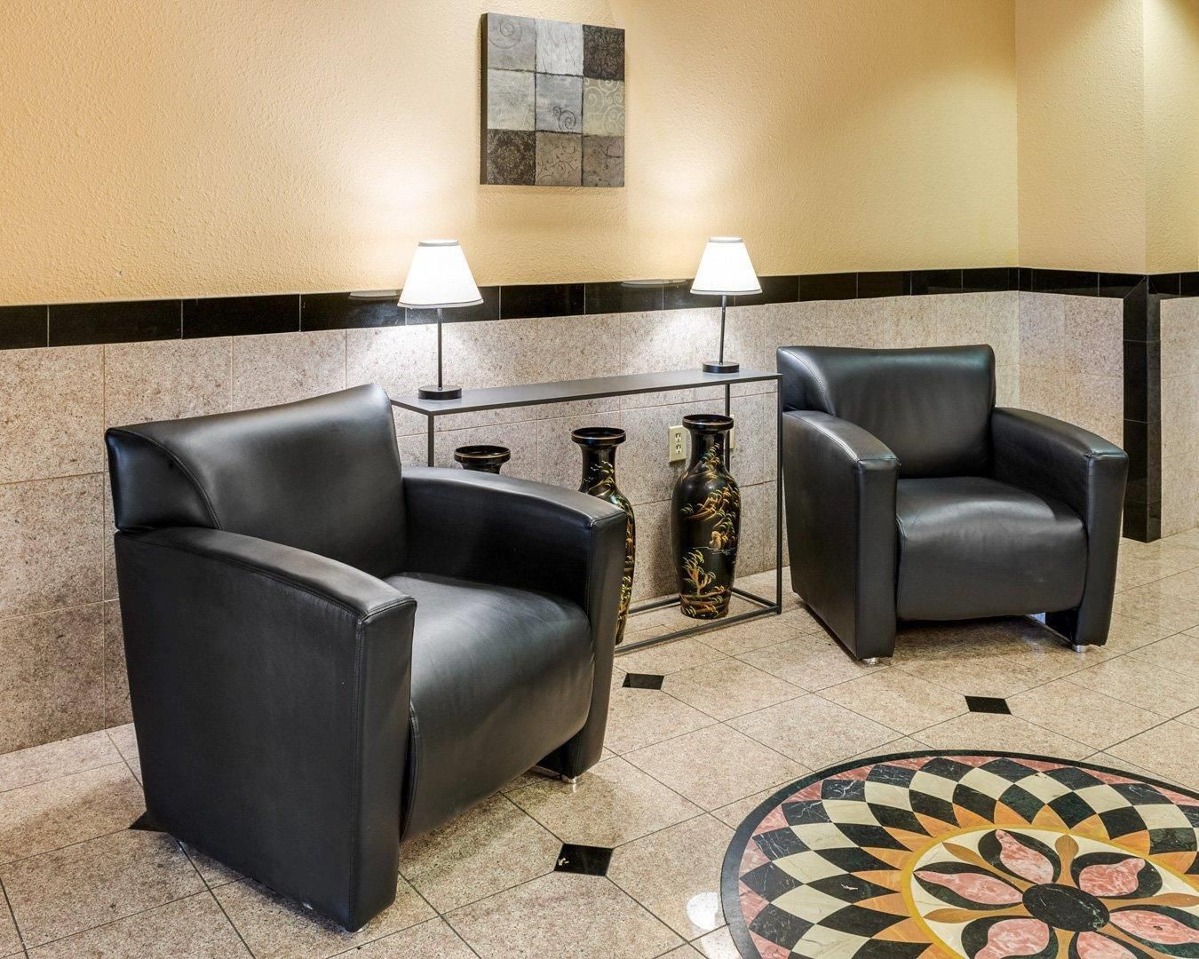 A lobby with two black leather armchairs, a small table with two lamps, and decorative vases.