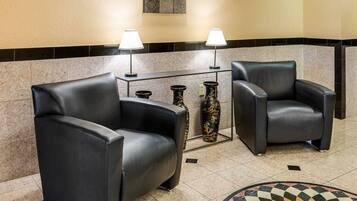 A lobby with two black leather armchairs, a small table with two lamps, and decorative vases.