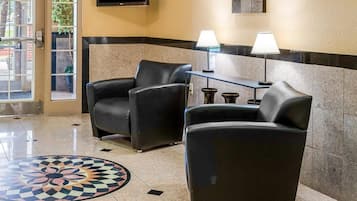 A lobby with two black leather armchairs, a small table with two lamps, a flat-screen TV mounted on the wall, and a patterned floor design.