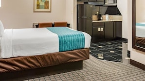 A hotel room with a bed, a kitchenette, and a bathroom. - Suburban Studios Avondale (Westwego)