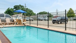 A swimming pool with a fenced area, lounge chairs, and a blue umbrella. - Suburban Studios Avondale (Westwego)