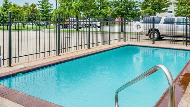 A rectangular swimming pool with a metal ladder on one side, surrounded by a black metal fence. - Suburban Studios Avondale (Westwego)