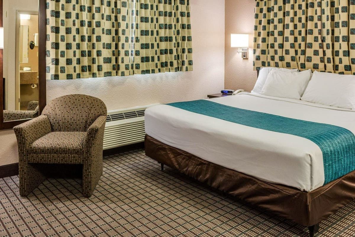 A hotel room with a bed, a chair, a mirror, and patterned curtains.