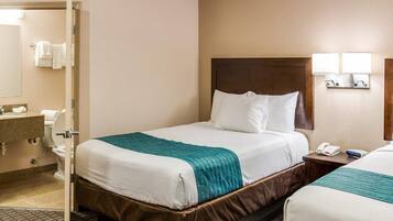 Una habitación de hotel con cama, mesita de noche y baño visible a través de una puerta abierta.