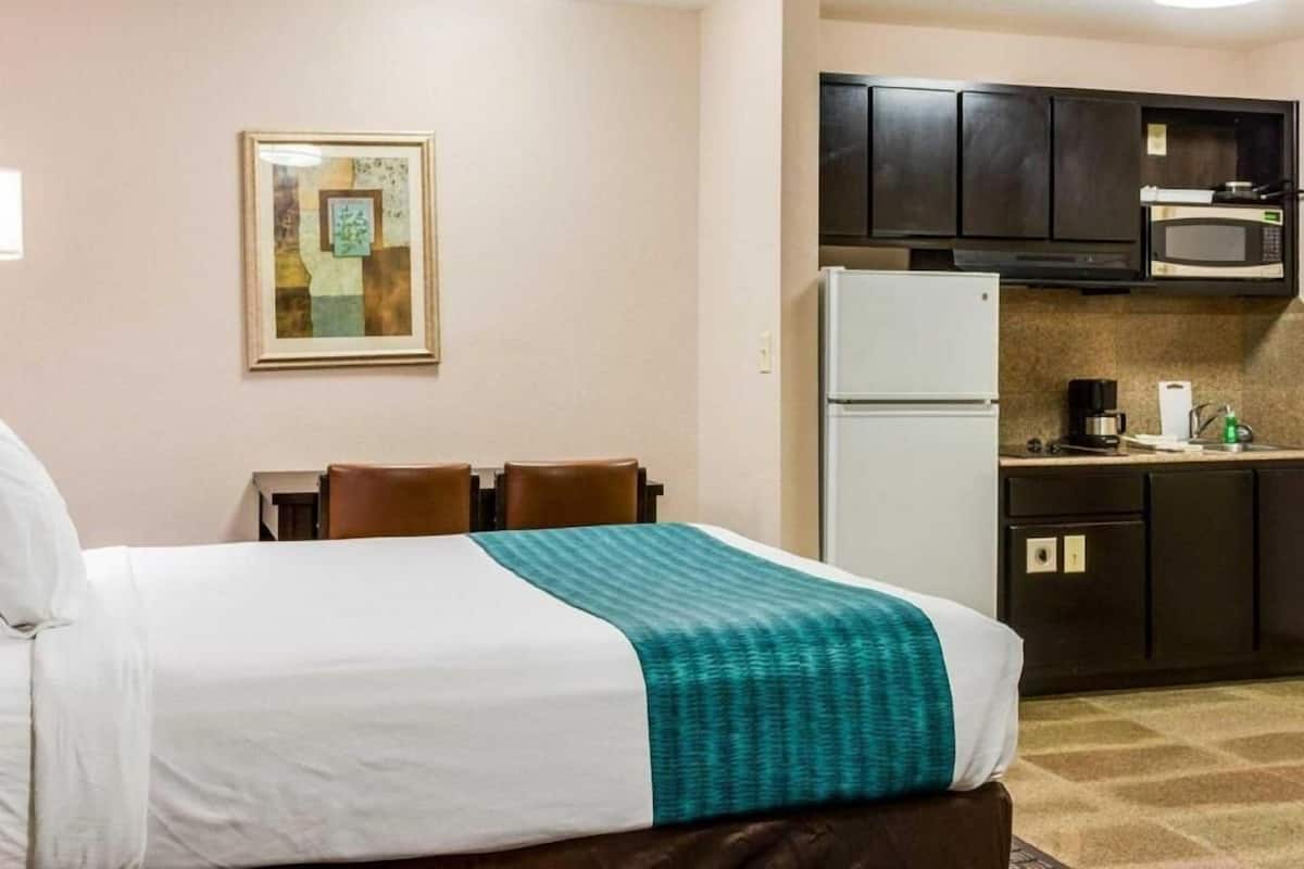 A hotel room with a bed, a small kitchenette, and a framed picture on the wall.