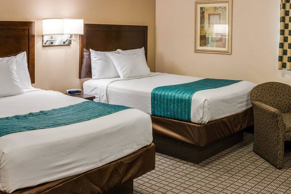 A hotel room with two beds, a nightstand, a lamp, a chair, and a framed picture on the wall.