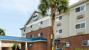 A hotel with a brick facade, a covered parking area, and a palm tree. - Suburban Studios Avondale (Westwego)