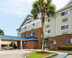 A hotel with a brick facade, a covered parking area, and a palm tree.