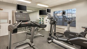 Une salle de sport équipée de machines de cardio, dotée d’un mur avec des miroirs et d’une grande fenêtre.