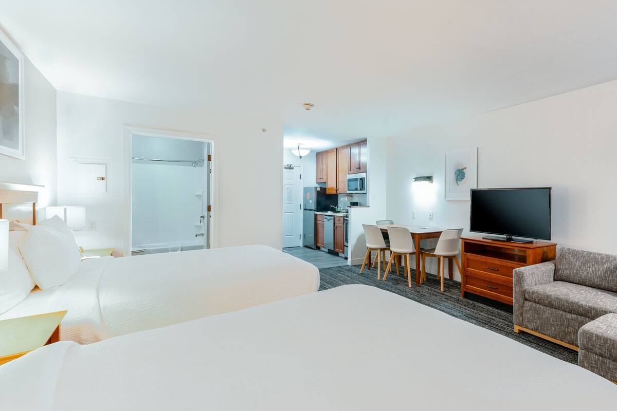Een hotelkamer met twee bedden, een televisie, een zithoek met stoelen en een keuken op de achtergrond.