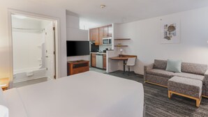 Une chambre d’hôtel comprenant un lit, une télévision, une kitchenette et un coin salon avec un canapé et un fauteuil.