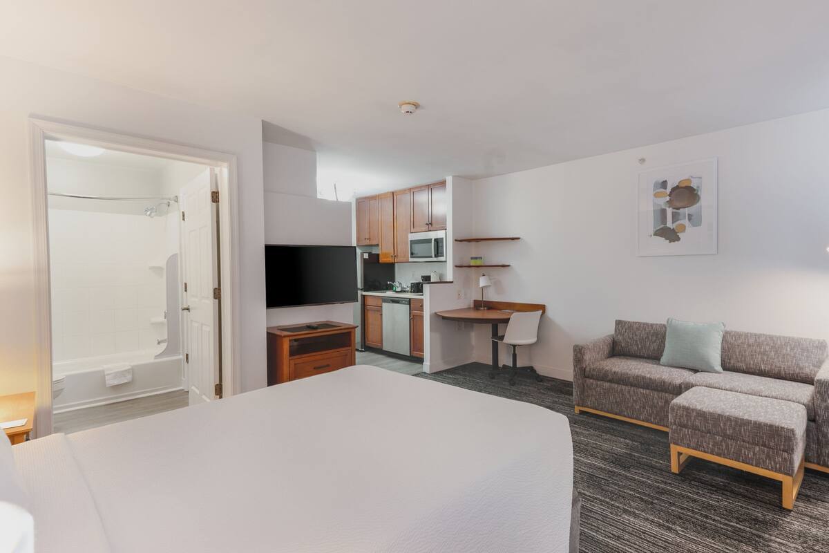 Hotelkamer met een bed, een televisie, een kitchenette en een zithoek met een bank en een stoel.