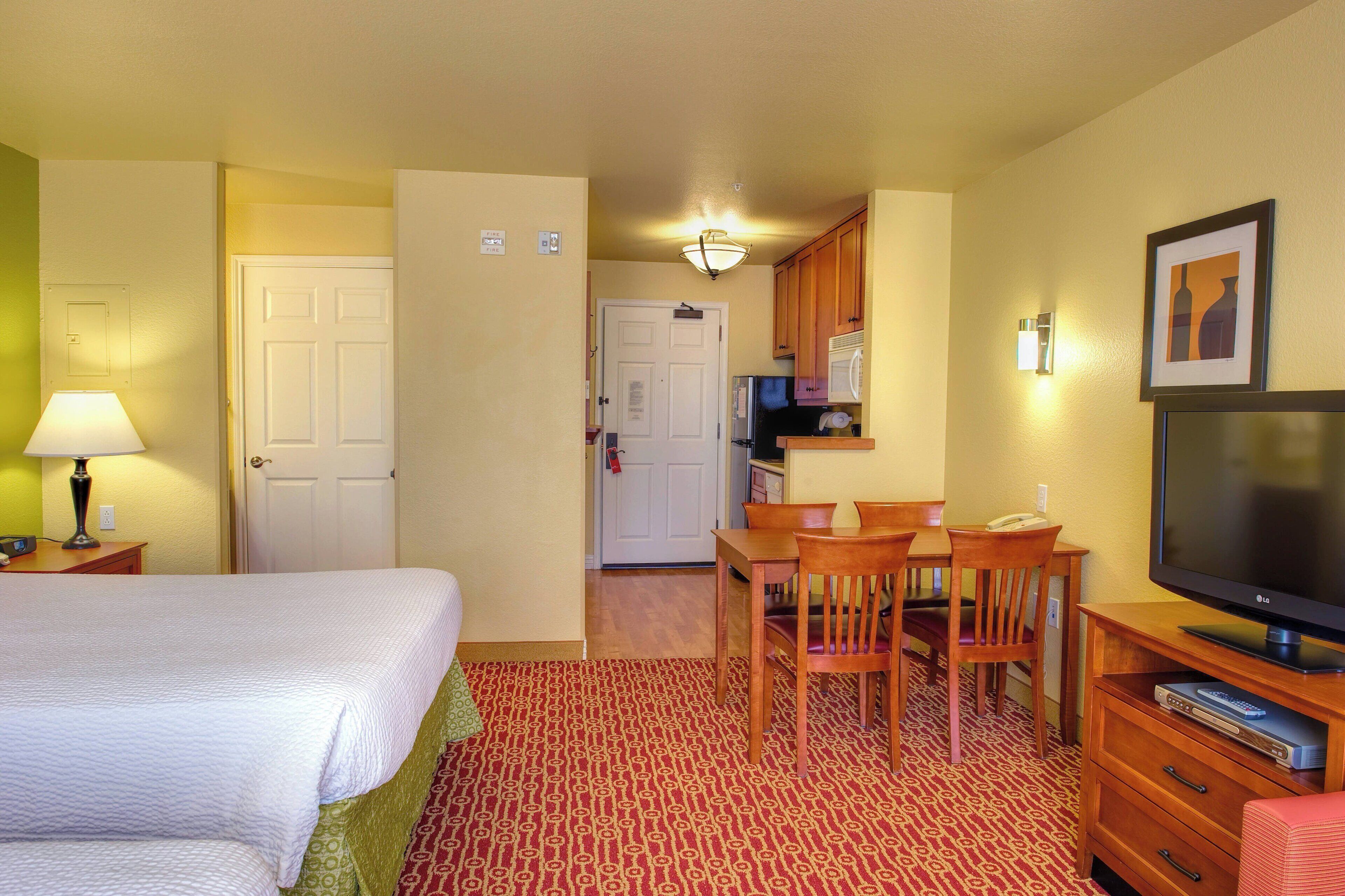 Une chambre d’hôtel comprenant un lit, un bureau avec une chaise, une télévision et une kitchenette.