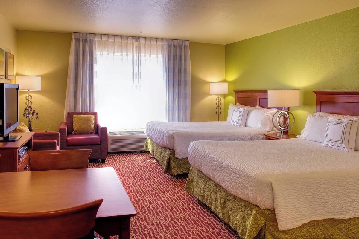 Hotelkamer met twee bedden, een bureau, een stoel, een televisie en een raam met gordijnen.