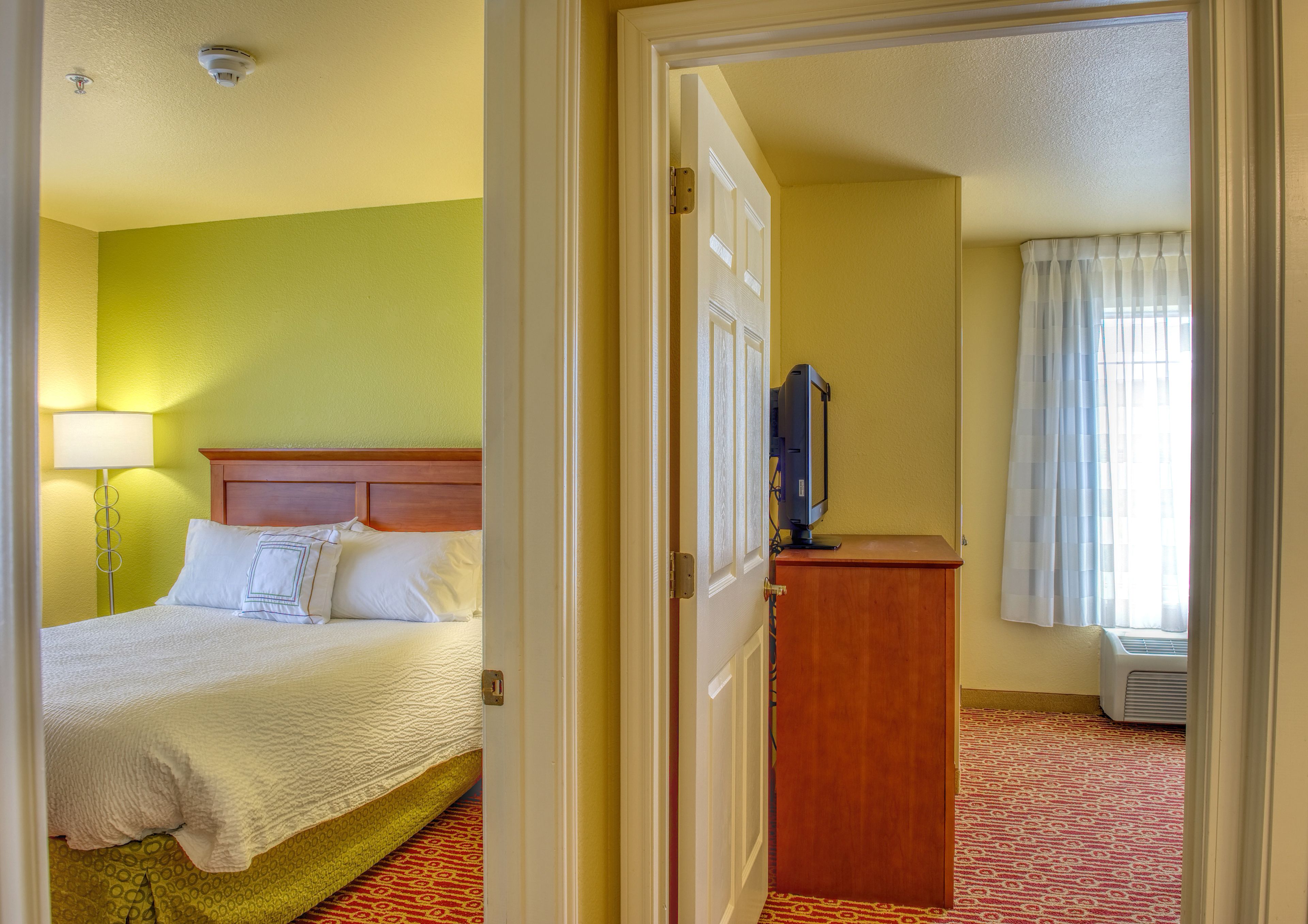 A hotel room with a bed, a desk, a lamp, and a window with curtains.