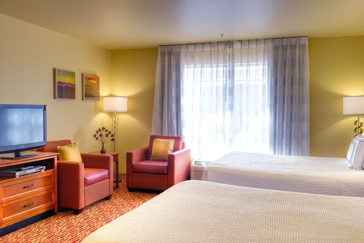 Een hotelkamer met een televisie, twee rode fauteuils, een bureau, een lamp en twee bedden.