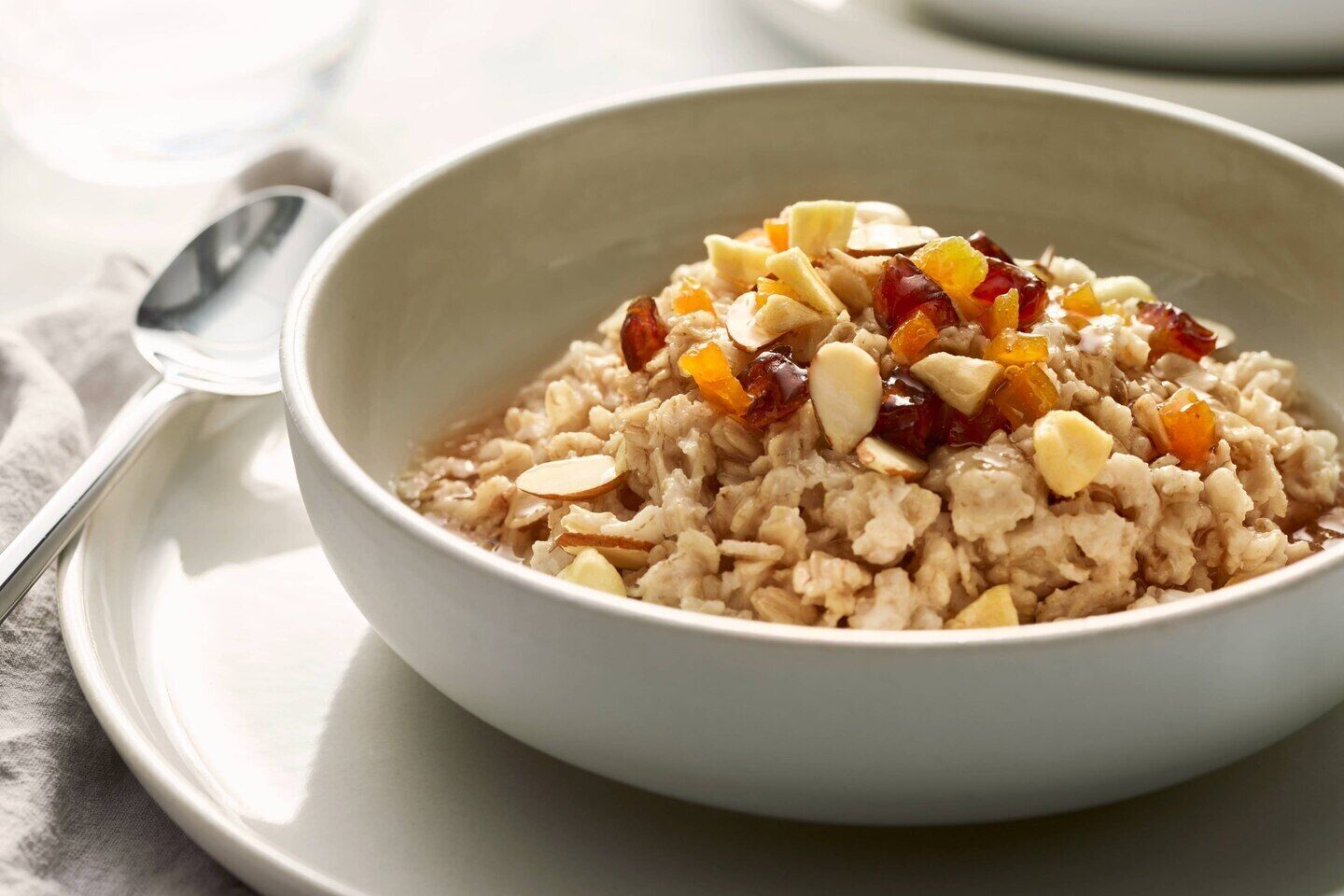 A bowl of oatmeal with almonds and dried fruit on a white plate.