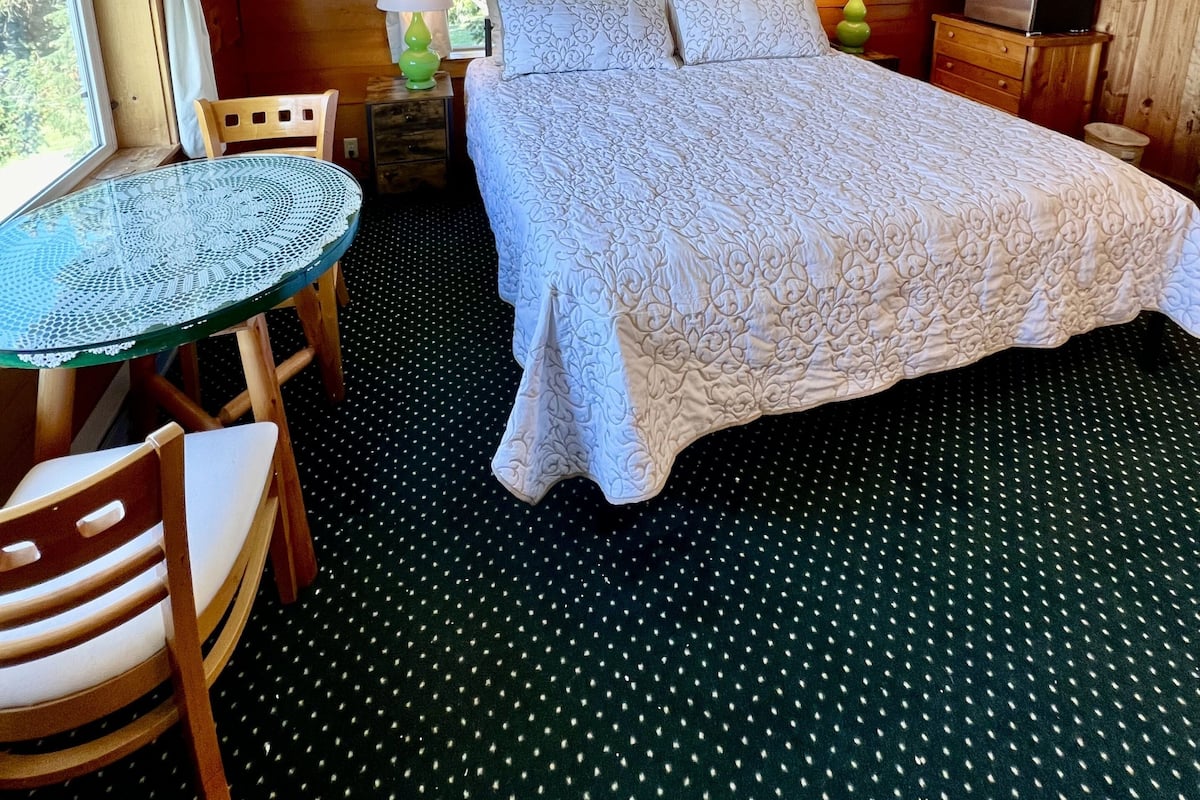 A cozy room with a bed, a small table, chairs, and a refrigerator.