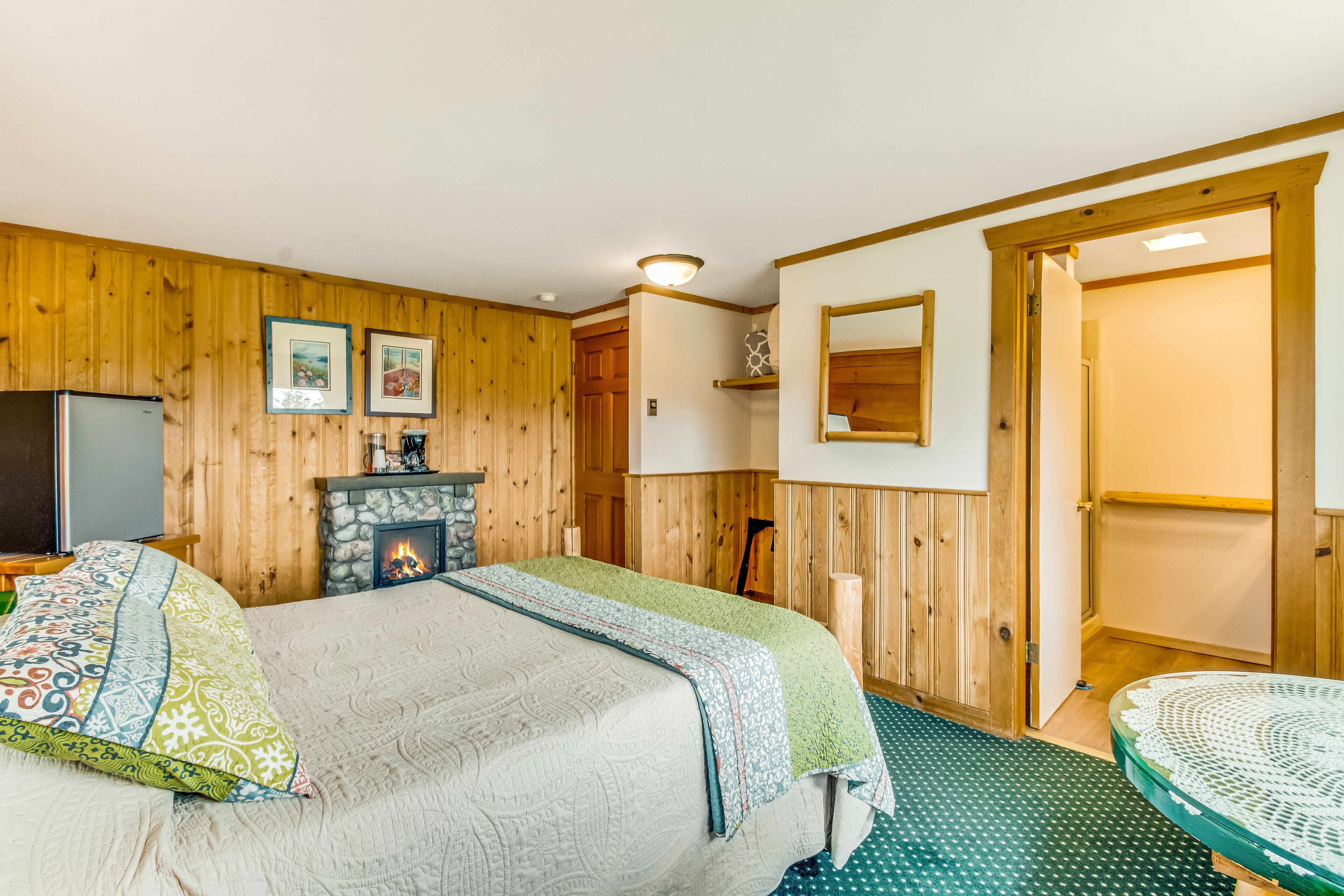 Um quarto acolhedor com cama, lareira, paredes de madeira e uma porta que dá para outro espaço.