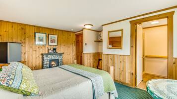 Um quarto acolhedor com cama, lareira, paredes de madeira e uma porta que dá para outro espaço.