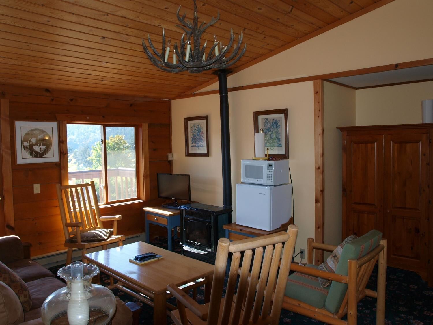 L’intérieur chaleureux d’un chalet avec des murs en bois, une table à manger, des chaises, un téléviseur, un four à micro-ondes et une cheminée.