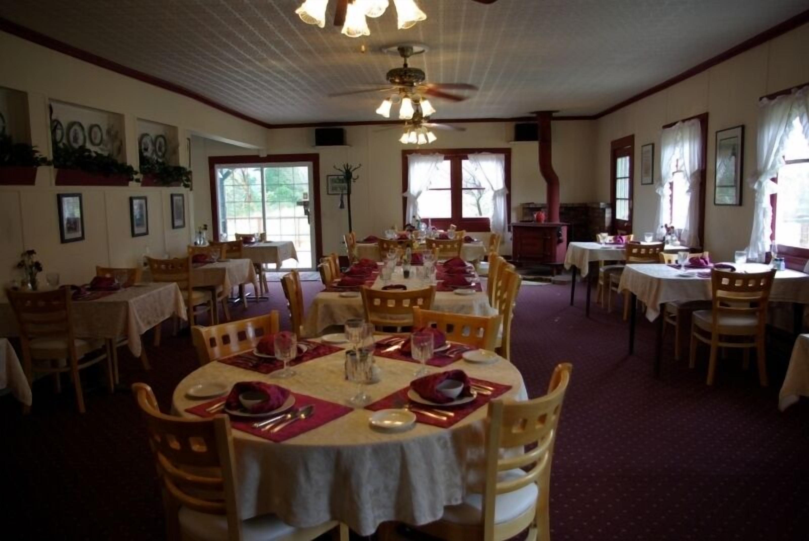 A dining area with round tables set for multiple guests, wooden chairs, and a ceiling fan.