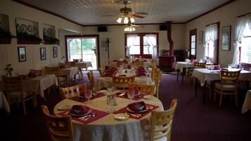 A dining area with round tables set for multiple guests, wooden chairs, and a ceiling fan.