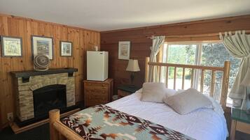 A wooden cabin bedroom with a stone fireplace, a bed with a patterned blanket, and framed pictures on the wall.