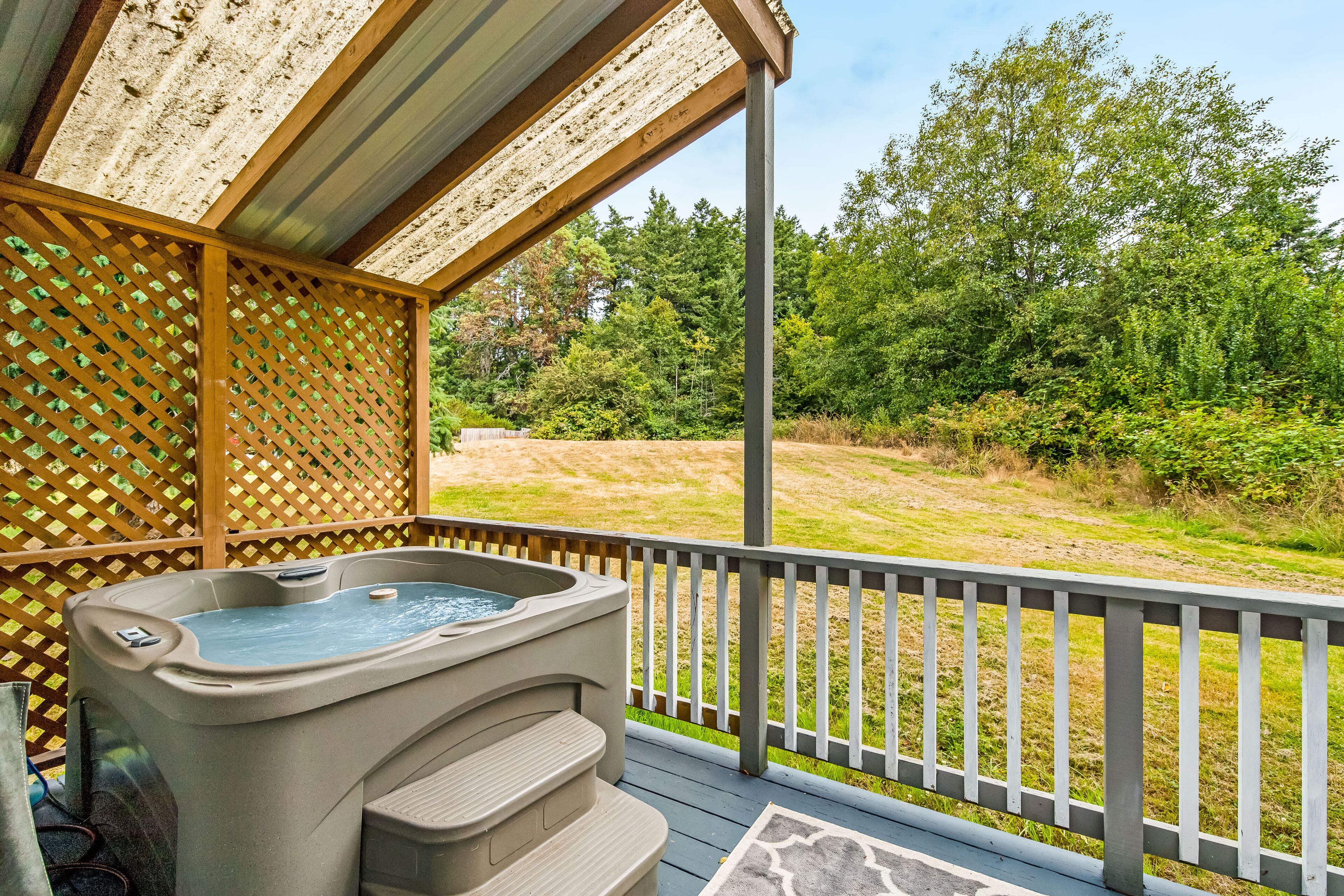A hot tub on a wooden deck with a view of a grassy area and trees.