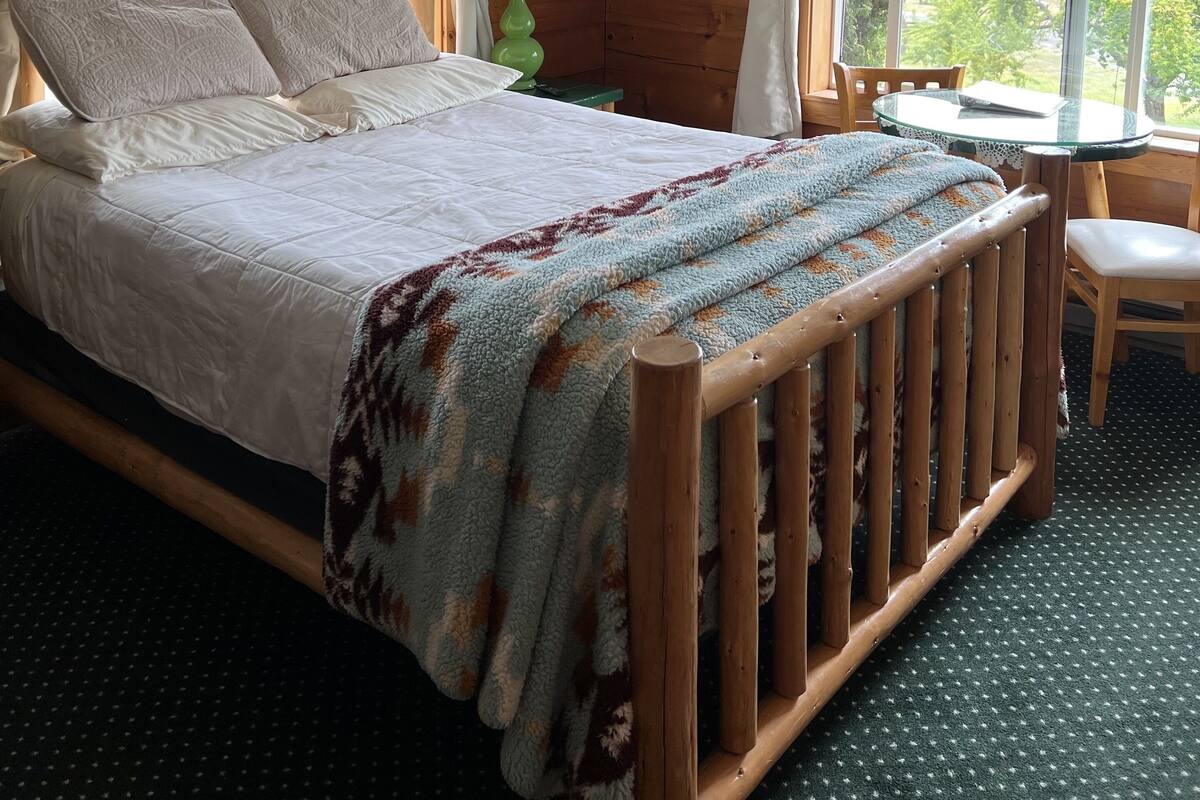 A wooden cabin bedroom with a bed, a small table, and a chair.