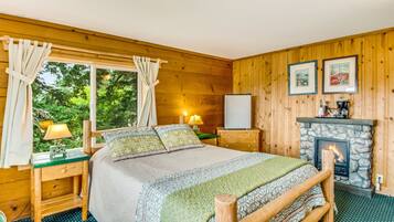 A cozy wooden cabin bedroom with a bed, nightstands, a fireplace, and a window with curtains.