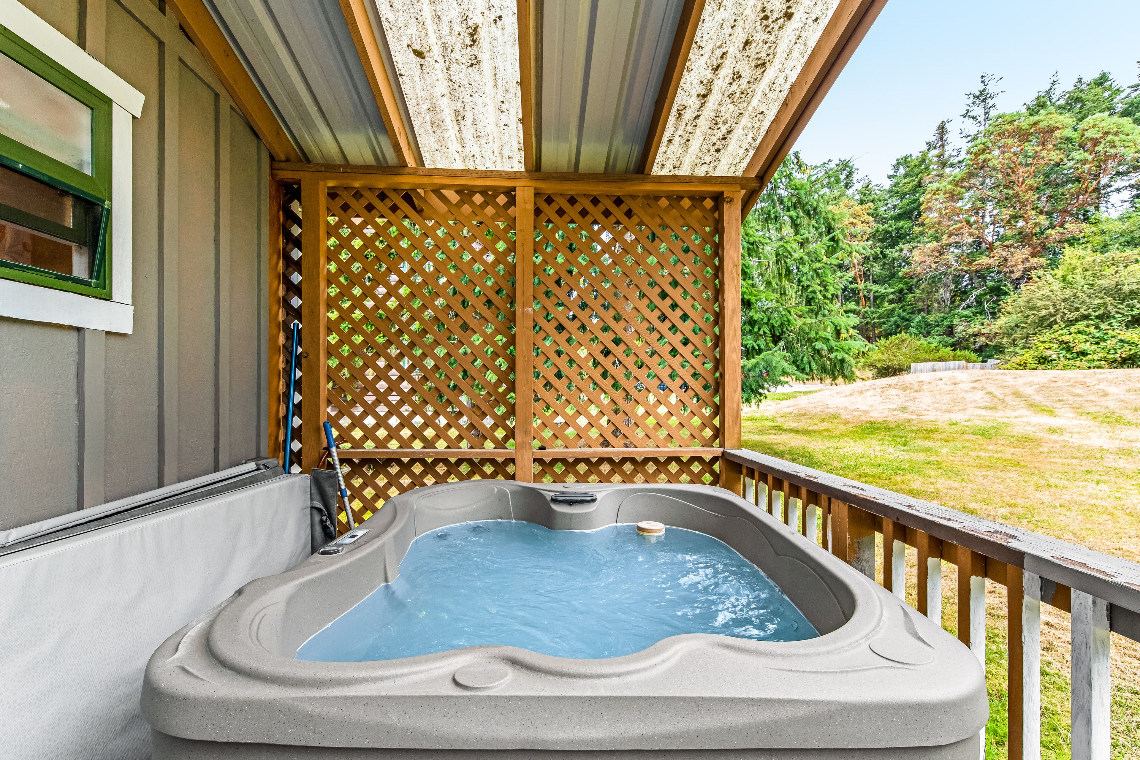 A hot tub on a wooden deck with a lattice backdrop and a view of a grassy yard and trees.