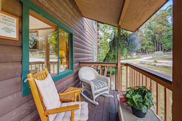A wooden cabin with a porch featuring rocking chairs, a table, and a potted plant.