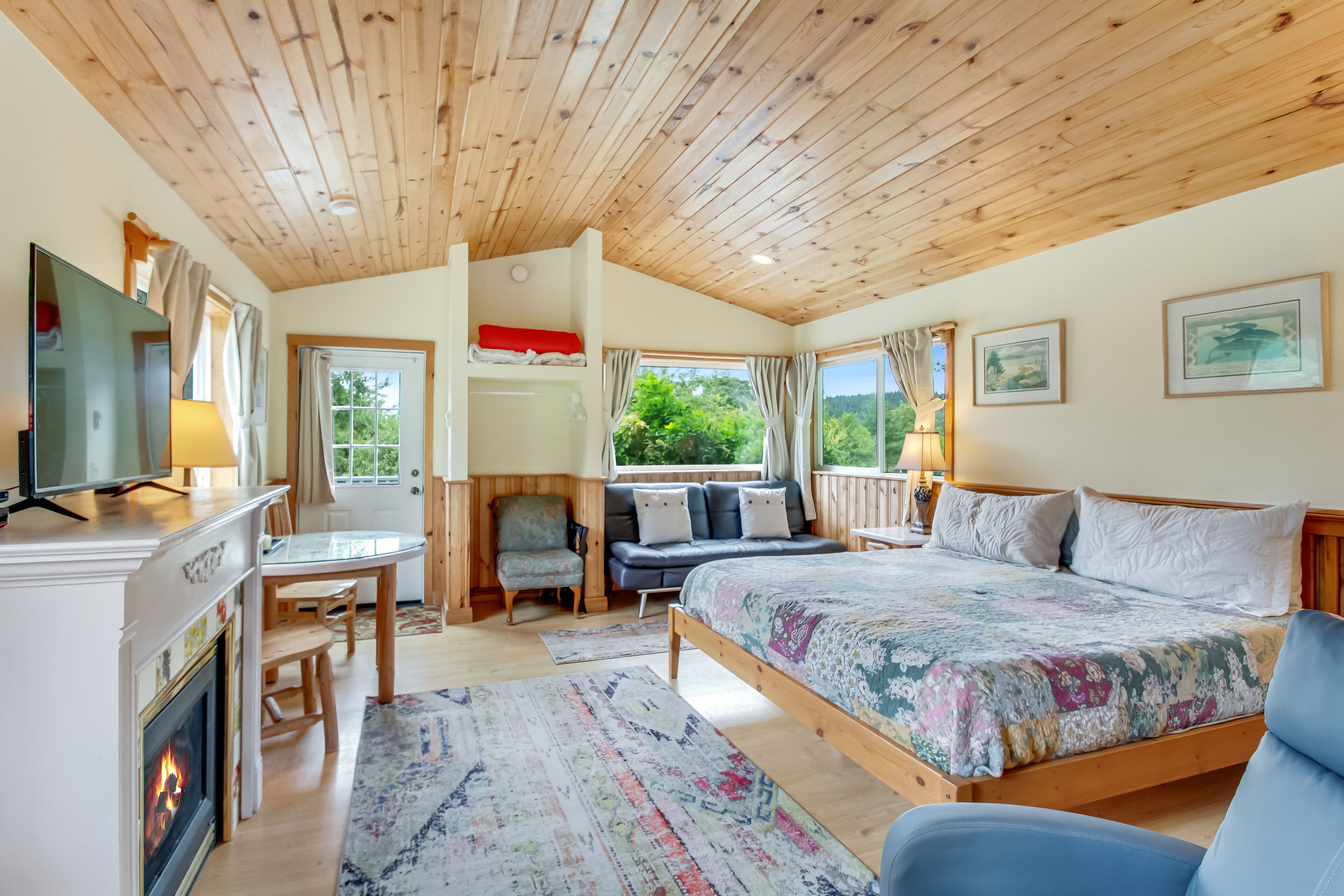 Une chambre confortable avec un plafond en bois, un grand lit, une télévision, une cheminée et une vue sur la verdure.