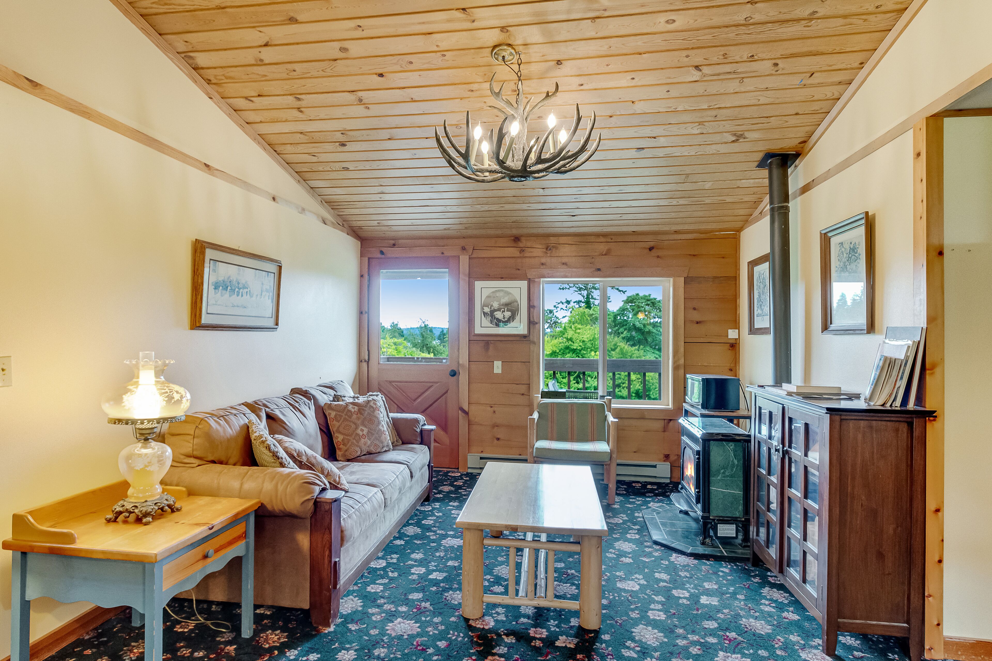 A cozy cabin interior with a wooden ceiling, a sofa, a table, a cabinet, and a fireplace.