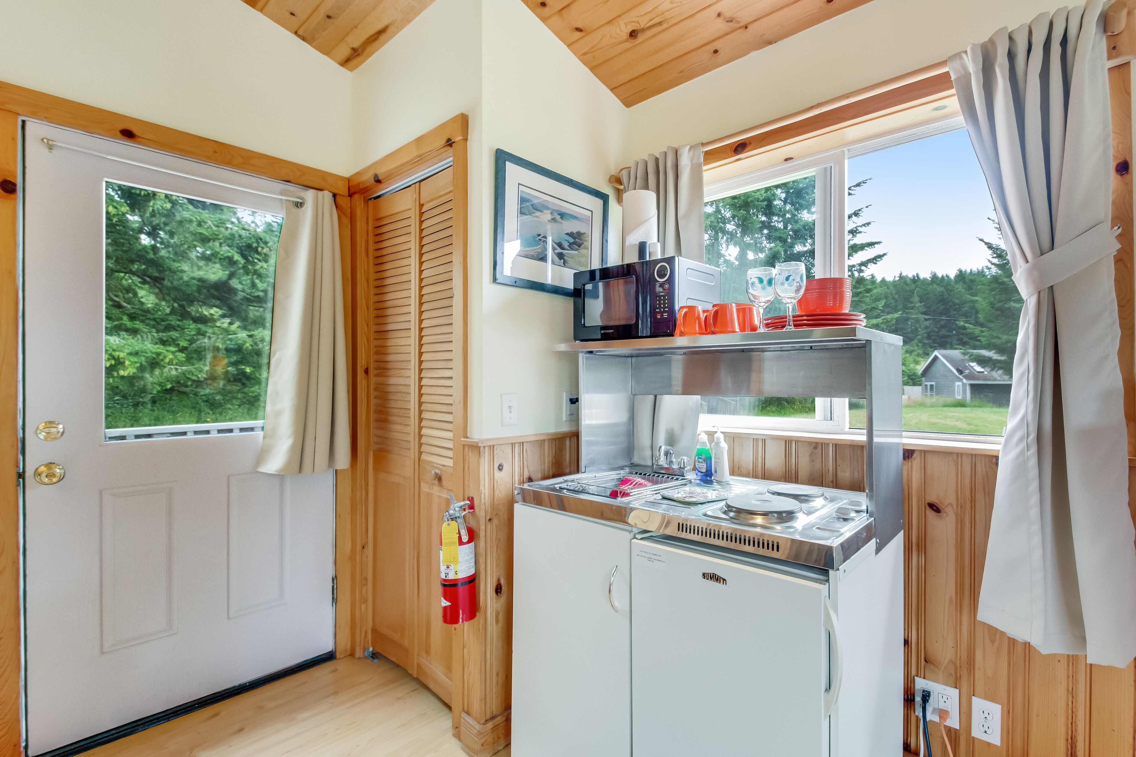 A compact kitchen with a microwave, toaster, and small refrigerator. A fire extinguisher is mounted on the wall.
