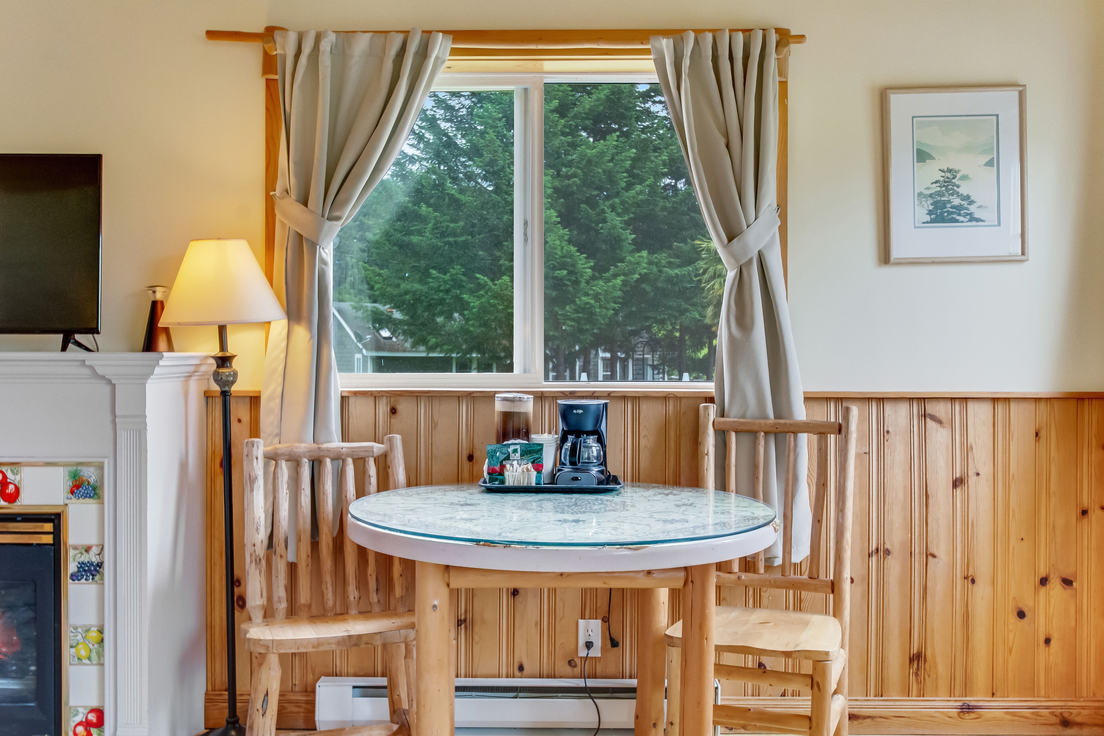 A cozy room with a round table, wooden chairs, a coffee maker, and a TV on a stand.