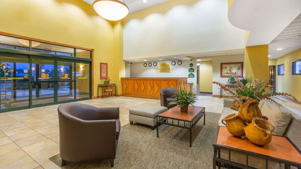 A lobby with a reception desk, seating area, and a large window overlooking the street. - Wingate by Wyndham West Monroe (West Monroe)