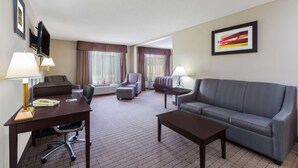 A hotel room with a desk, two chairs, a sofa, and a television. - Wingate by Wyndham West Monroe (West Monroe)