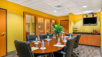 Un salón de conferencias con una mesa de madera, sillas negras y botellas de agua.