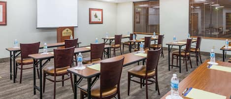 A conference room with multiple tables and chairs, equipped with water bottles and notepads.